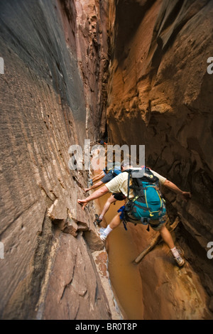 Three people stemming between two walls above water in slot canyon, Utah. Stock Photo