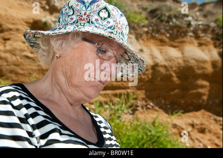 Elderly lady wearing a hat sitting outdoors on a summers day looking serious. Stock Photo