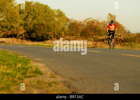 A woman is road cycling atsunset at Iona Beach, Richmond, British Columbia, Canada. Stock Photo