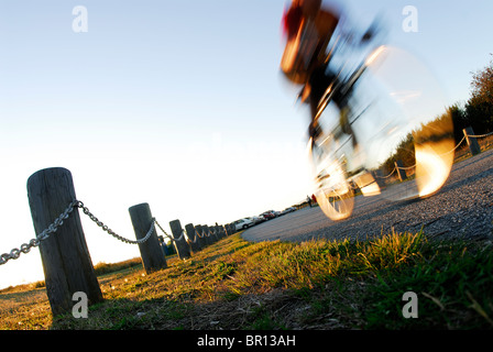 A woman is road cycling atsunset at Iona Beach, Richmond, British Columbia, Canada. (blurred motion) Stock Photo