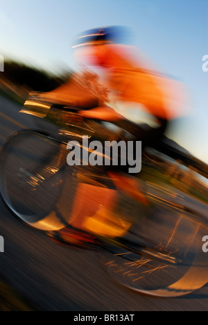 A woman is road cycling atsunset at Iona Beach, Richmond, British Columbia, Canada. (blurred motion) Stock Photo