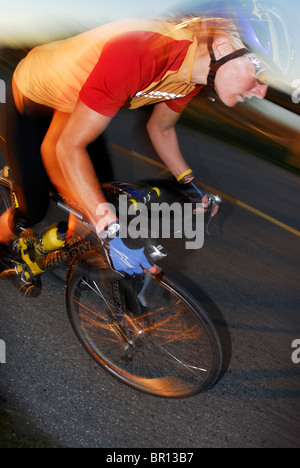 A woman is road cycling atsunset at Iona Beach, Richmond, British Columbia, Canada. (blurred motion) Stock Photo