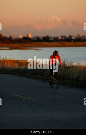 A woman is road cycling atsunset at Iona Beach, Richmond, British Columbia, Canada. Stock Photo