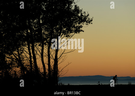 A woman is road cycling atsunset at Iona Beach, Richmond, British Columbia, Canada. (silhouette) Stock Photo