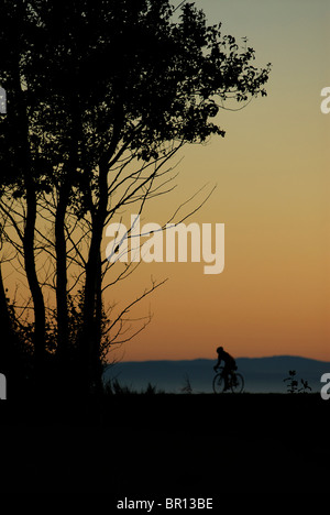 A woman is road cycling atsunset at Iona Beach, Richmond, British Columbia, Canada. (silhouette) Stock Photo