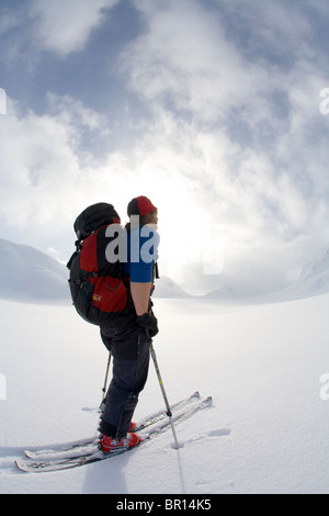 Backcountry skier crosses glacier under late day stormy sky.