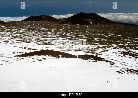 A distant view of two snowboarders walking up the snow covered slope of a volcano, Hawaii, USA. Stock Photo