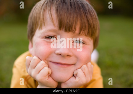 Small Blue Eyed Boy in Yellow T-Shirt Lying on Green Grass Relaxing with a Happy Smile Stock Photo