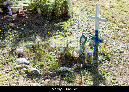 overgrown grave of young Makah Indian girl marked with figurines plastic flowers & simple wooden cross in Makah cemetery Stock Photo
