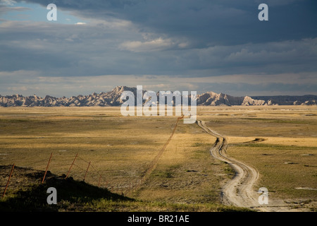 A dirt road winds through open fields before ending in the mountains of Badlands National Park. Stock Photo