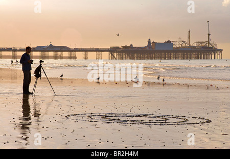 Silhouette of the Palace Pier now called Brighton Pier and photographer, Brighton. Low tide at sunset. East Sussex, England Stock Photo