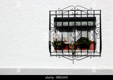 White wall with an off-centre window protected by wrought iron grille; flowerpots behind; taken  in Las Negras, Spain Stock Photo