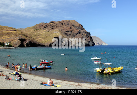 Landscape view of beach at Las Negras Spain showing people and boats in teh foreground with black rocky headland; deep blue sea Stock Photo