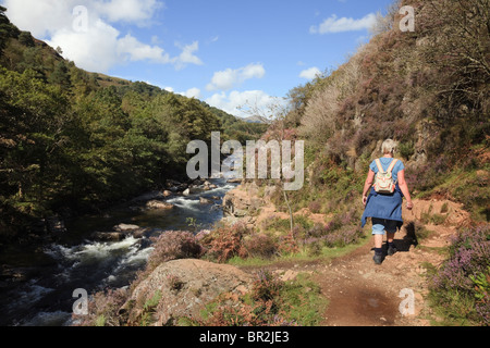 Woman walker walking on riverside path in Afon Glaslyn River gorge in Aberglaslyn Pass in Snowdonia National Park. Beddgelert, North Wales, UK. Stock Photo
