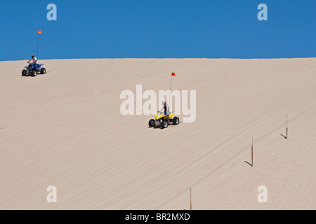 Two sporting boys driving ATV all terrain vehicle down sandy dunes in Michigan MI USA low angle from below outside horizon U.S.lifestyle hi-res Stock Photo