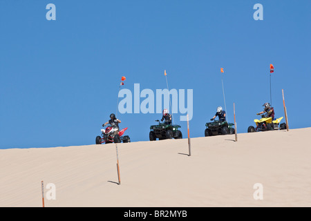 A teenagers driving ATV all terrain vehicle down sandy dunes four sporting boys in Michigan MI USA US lifestyle life from below outside horizon hi-res Stock Photo