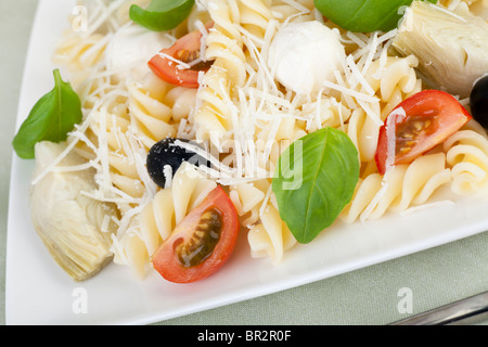 Fusilli pasta with black olives, mozzarella cheese, artichoke hearts and tomato slices, topped with fresh basil leaves. Stock Photo