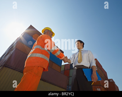 manual worker and businessman shaking hands near shipping containers Stock Photo