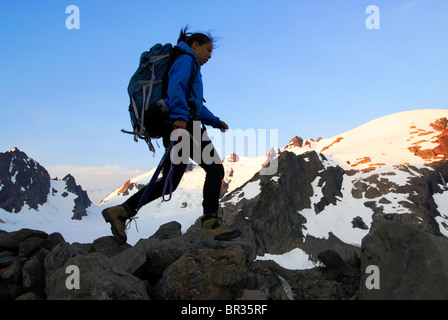 A woman hiking along a lateral morraine at sunrise accross from the summit of Mt. Olympus in Olympic National Park in Washington Stock Photo