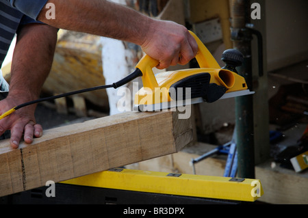 Carpenter using an electric plane on a piece of oak Stock Photo