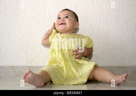 Tulum, Quintana Roo/Mexico - May 4: Full lenght baby girl in green dress seating on the floor against white wall Stock Photo