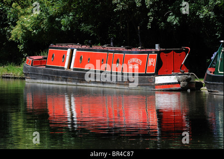 A bright red narrowboat moored below trees on the Grand Union Canal Stock Photo