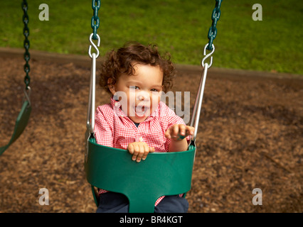 Mixed race child sitting in swing laughing Stock Photo