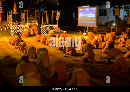 Novice monks bow at alter and digital projector shows Microsoft screen saver prior to multi-media presentation during ceremony a Stock Photo