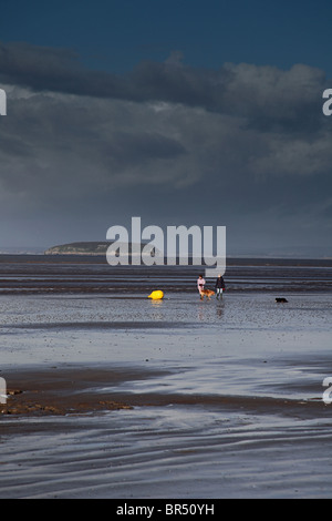Dog walkers at low tide at Berrow on the Bristol Channel coast, Somerset, England, UK.  Steep Holm island beyond Stock Photo
