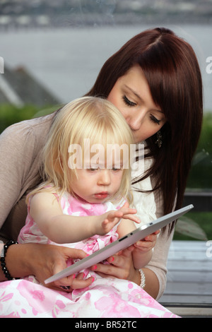 Mother and her two year old daughter using an Apple iPad in their home. Stock Photo