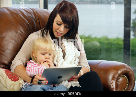 Mother and her two year old daughter using an Apple iPad in their home. Stock Photo