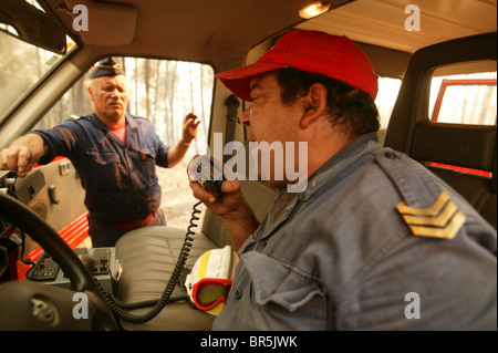 Two firemen on a firetruck talk on the radio to come up with a strategy to extinguish a wildfire in a forest in central Portugal Stock Photo