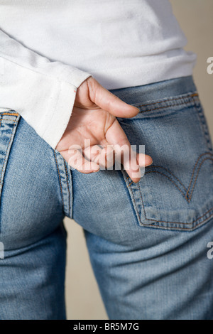 Color image of attractive woman wearing a pair of jeans and white shirt with crossed fingers behind her back.