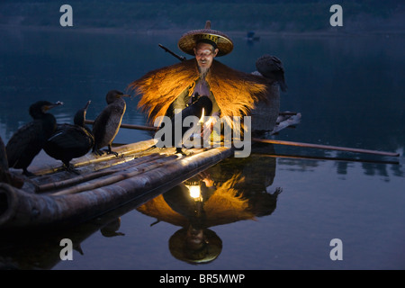 Fisherman wearing straw coat fishing with cormorants on bamboo raft on Li River at dusk, Yangshuo, Guangxi, China Stock Photo