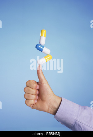 man balances three giant pills on his thumb Stock Photo