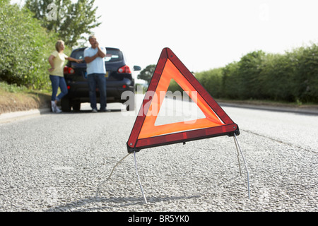Couple Broken Down On Country Road With Hazard Warning Sign In Foreground Stock Photo