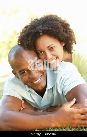 Portrait Of Young Couple Laying On Grass In Park Stock Photo