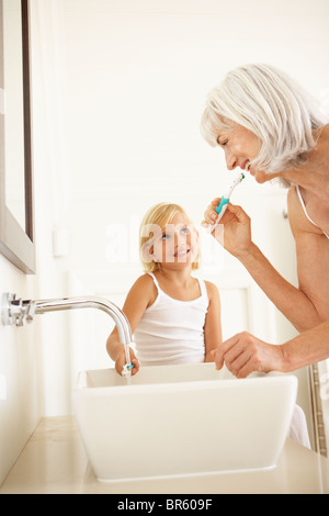 Grandmother Brushing Teeth In Bathroom With Granddaughter Watching Stock Photo
