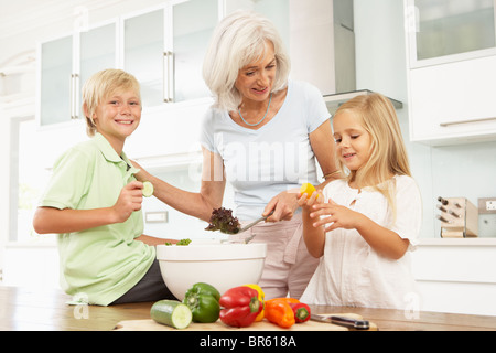 Grandchildren Helping Grandmother To Prepare Salad In Modern Kitchen Stock Photo