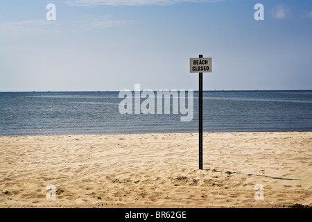 'Closed Beach' sign in the sand with oil rigs on the horizon along the Gulf Coast. Stock Photo