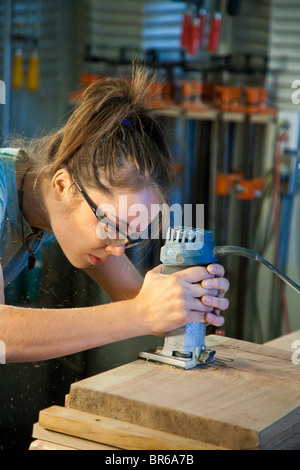 Young female apprentice sanding a cabinet part in a woodshop. Stock Photo