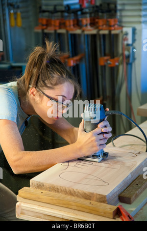 Young female apprentice using a router in a wood-shop. Stock Photo