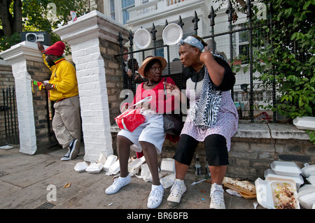 Two women gossiping and chatting together sitting on wall in the street Stock Photo