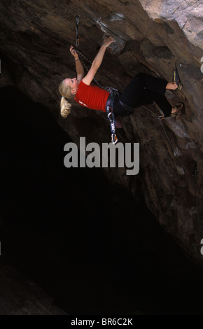 A young woman rock climbing places a rope in an anchored bolt on an overhanging route. Stock Photo