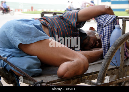 A poverty stricken handicapped amputee man sleeps in a wheelchair in Phnom Penh, Cambodia. Stock Photo