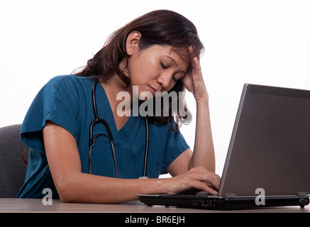 Attractive thirties asian nurse doctor working on laptop with a headache Stock Photo
