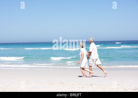 Senior Couple On Holiday Running Along Sandy Beach Stock Photo