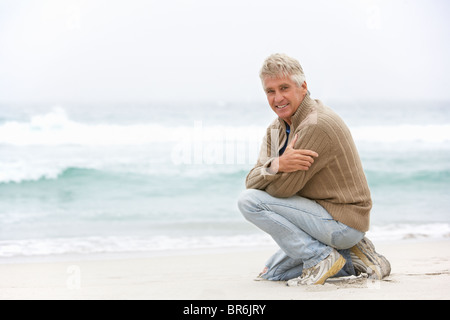 Senior Man On Holiday Kneeling On Winter Beach Stock Photo