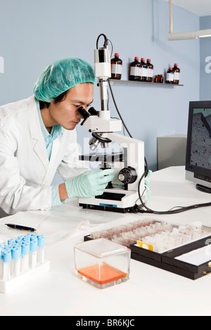 A lab technician looking into a microscope in a laboratory Stock Photo