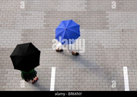 Two women with umbrellas walking through a parking lot Stock Photo